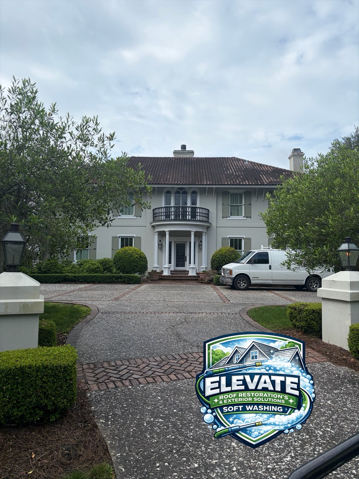 Before roof soft washing: two-story stucco house with a clay tile roof and a round balcony, the tiles dark with algae, Elevate logo in the corner