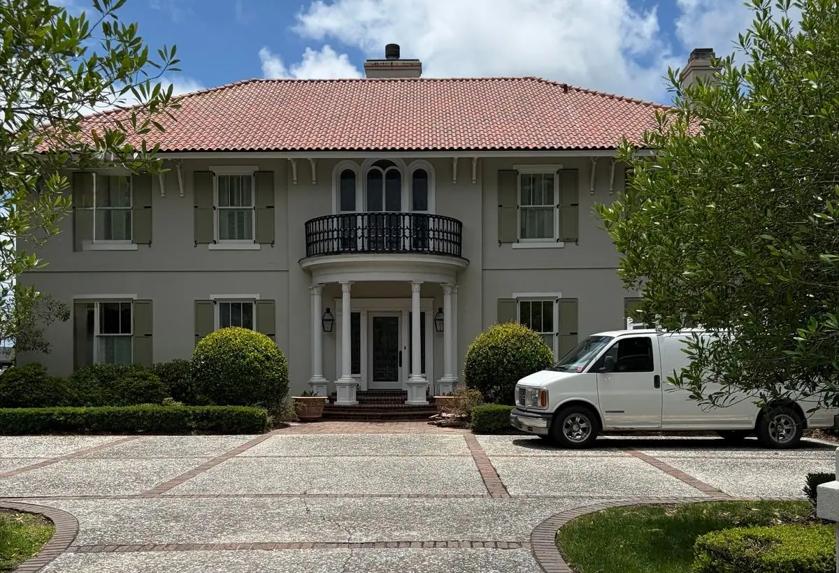 After roof soft washing: the same two-story stucco house with a clay tile roof and a round balcony, roof clean