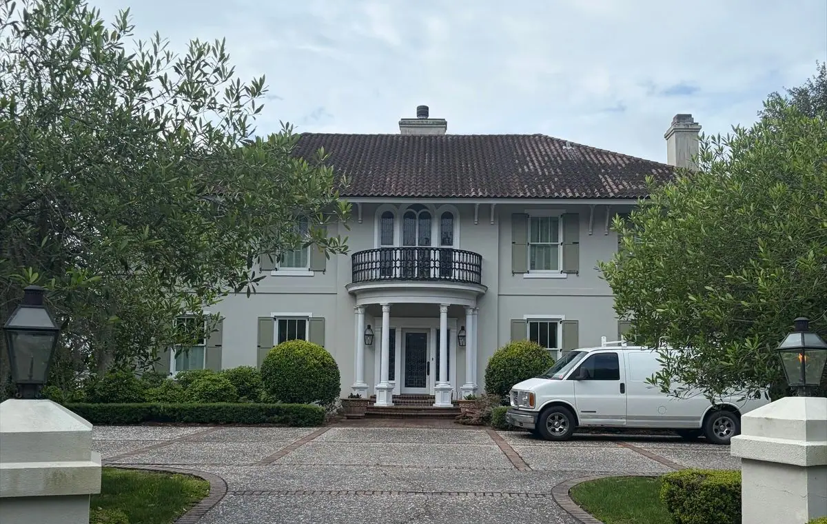 Before roof soft washing: two-story stucco house with a clay tile roof and a round balcony, roof dark with algae streaks