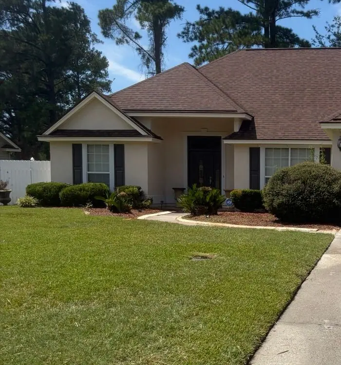 After roof soft washing: stucco ranch house with a brown shingle roof and a front lawn, roof clean