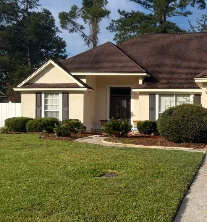 Before roof soft washing: stucco ranch house with a brown shingle roof and a front lawn