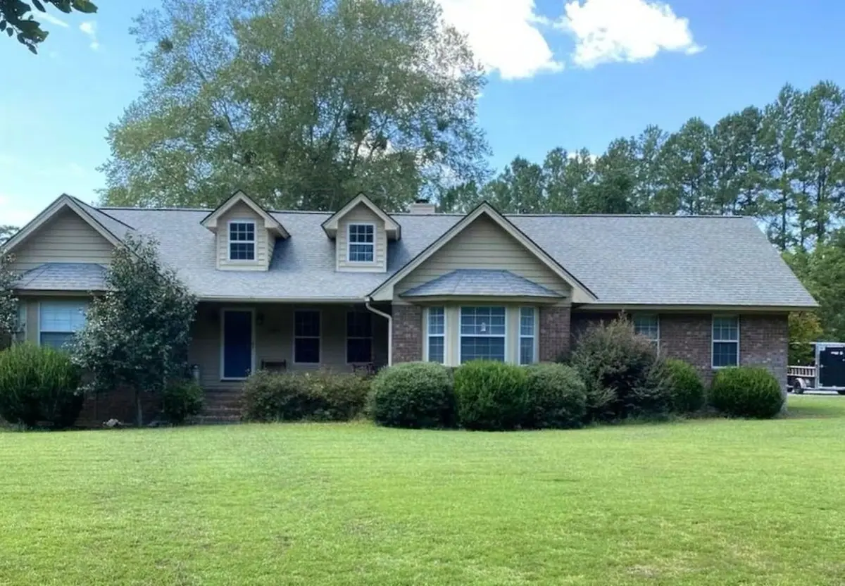 After roof soft washing: the same brick ranch house with two dormers and an asphalt shingle roof, roof clean