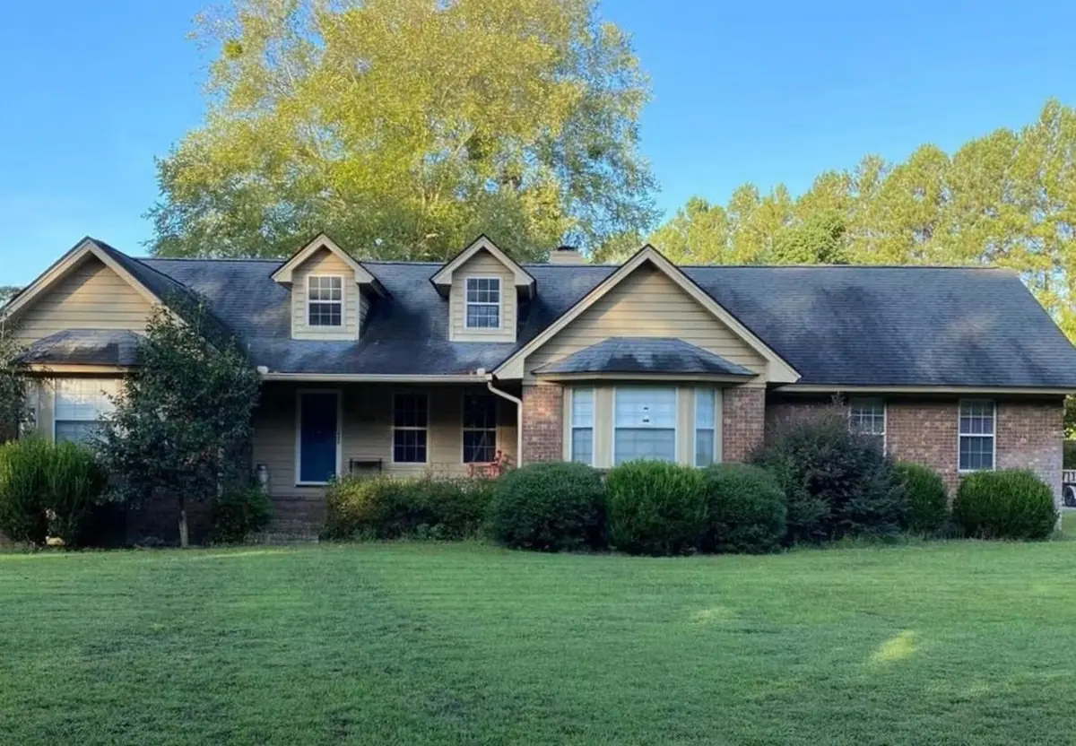 Before roof soft washing: brick ranch house with two dormers and an asphalt shingle roof, roof dark with algae streaks